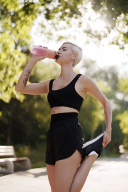 Bir fitness meraklısı parkta koştuktan sonra su molası verir.