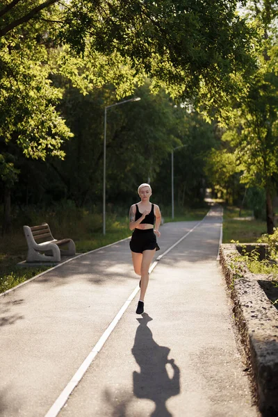 A female athlete runs on a sun-drenched park lane lined with trees