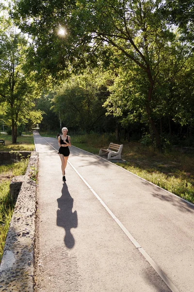 A runner strides forward on a park path with early morning sun peeking through the trees