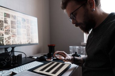 Nişanlı bir fotoğrafçı fotoğraf negatiflerinin detaylarını yakından incelemek için bir büyüteç kullanır.