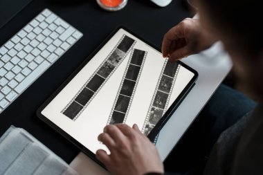 Bir fotoğrafçı dijital tablet üzerinde film negatiflerini inceleyerek, stüdyosundaki modern teknolojiyle geleneksel fotoğrafçılığı birbirine bağlar.