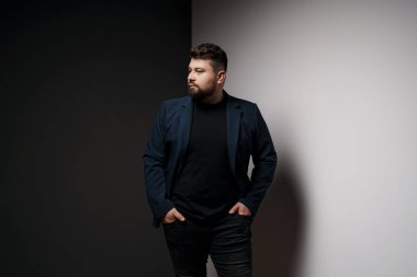 Kendine güvenen, sakallı bir adam elleri kalçasında, şık, modern bir spor ceket giyer.