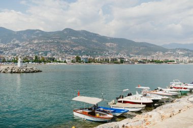 Sakin sulara yanaşan tekneler berrak bir gökyüzünün altında manzaralı bir şehir zeminine sahipler.