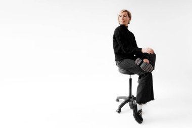 Gösterişli siyah bir elbise içinde düşünceli bir profesyonel, bir ofis taburesinde oturuyor, çağdaş zarafeti somutlaştırıyor.