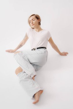 Genç bir kadın sükuneti meditasyon pozunda bulur. Hafif yıkama kotu ve yumuşak beyaz bir tişörtle örtülüdür.