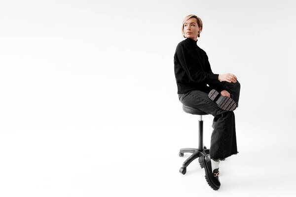Задумчивый профессионал в гладком черном ансамбле сидит на офисном стуле, воплощая современную элегантность