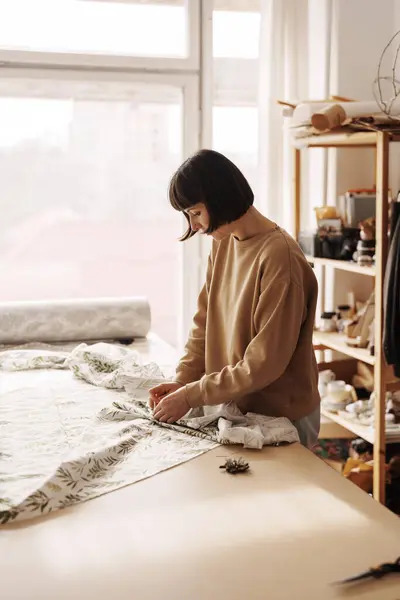 ファブリックや工芸品に囲まれた明るいワークショップで縫う女性 — ストック写真