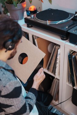Audiophile with headphones selects a vinyl record from a shelf to play on a turntable. clipart