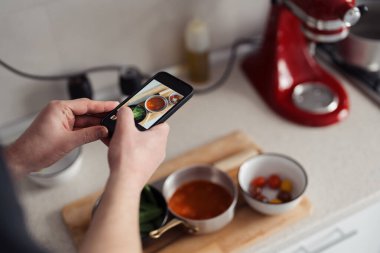 Ev yemeklerini telefonla çeken kişinin omuz üstü görüntüsü..