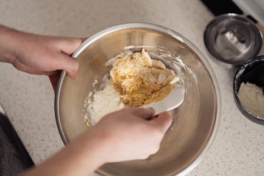 Mutfak tezgahında metal bir kasede hamur karıştıran ellerin yakın çekimi..