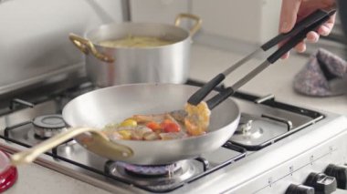Gaz ocağındaki tavada taze sebzelerle sağlıklı bir yemek pişiren biri. Ev yemeği, sağlıklı beslenme ve yaşam tarzı. Kızartma tavasına odaklan..
