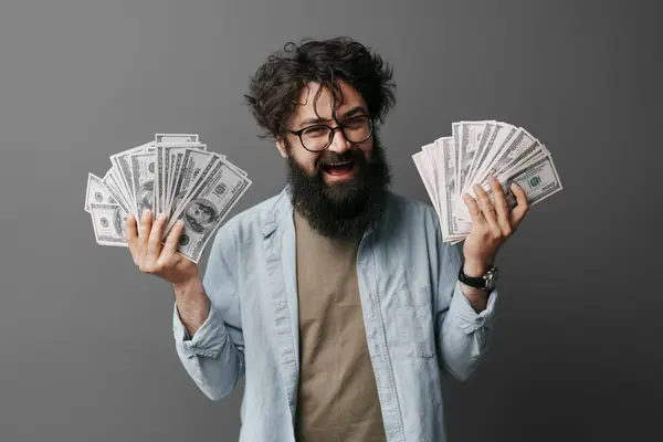 偶然服を着た男は中立的な背景に立って 両手で現金を抱えています このイメージは 大邸宅の顔を見せることなく 成功の概念を伝えます ストック画像