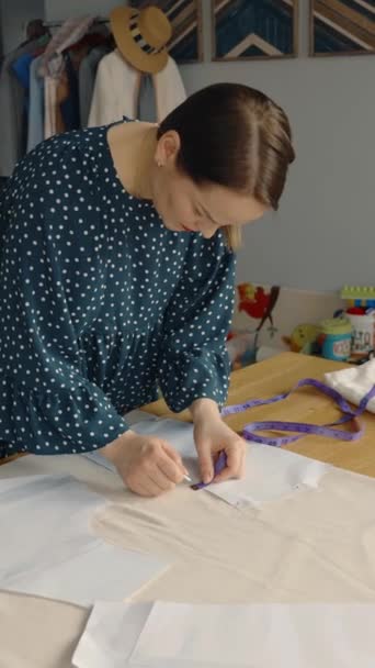 縫製アイテムや衣服に囲まれた彼女のワークショップでドレスパターンとファブリックで作業する女性のテーラー — ストック動画