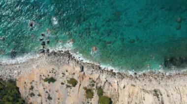 Bir drondan yakalanan turkuaz mavi denizle karşılaşan kayalık bir kıyı manzarası manzaranın doğal güzelliğini ve dokusunu vurguluyor..