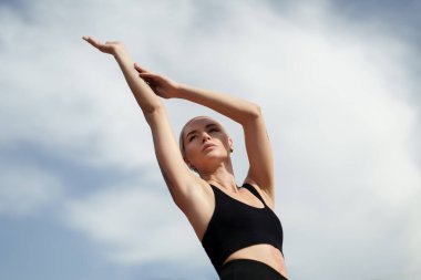 Genç bir sporcu, açık hava yoga seansı sırasında sağlığını ve sağlığını somutlaştıran mavi gökyüzüne doğru esniyor..