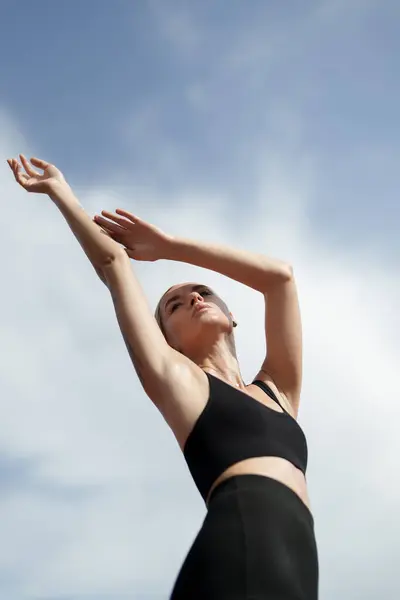 フィットネスの服装の若い女性は 明確な青い空の背景で腕を上に伸ばし 平和と幸福を示しています ストック画像