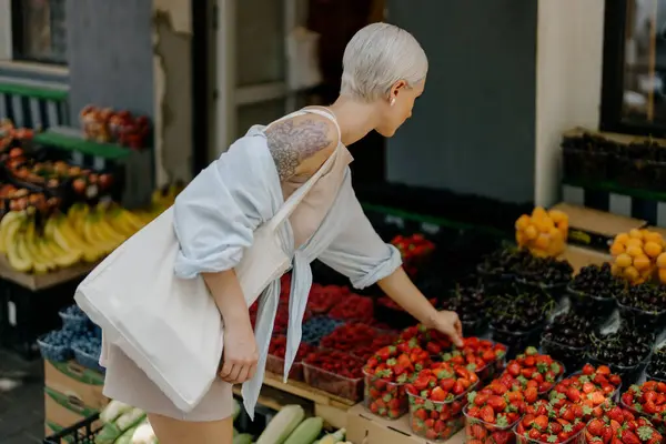 토트백을 여성은 다양한 생산품을 다채로운 가판대에서 신선한 과일을 선택하고 있습니다 로열티 프리 스톡 이미지