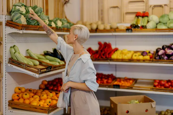 세련된 여성은 시장에 제품의 배열에서 신선한 야채를 선택합니다 스톡 사진