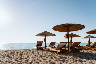Güneşli bir günde, saman şemsiyeli ve ahşap sandalyeli plaj sahnesi güneşli bir günde, yaz ve tatil kavramları için mükemmel..