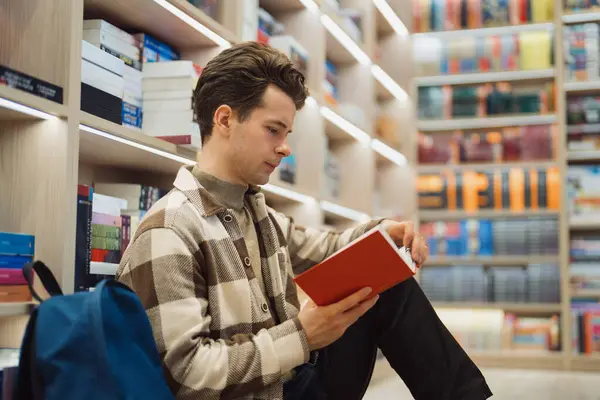 Focused Young Man Reads Red Book Library Surrounded Shelves Filled Royalty Free Stock Photos