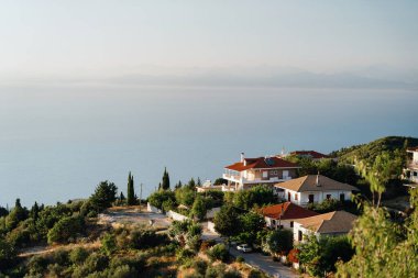 Güneşin sıcacık parıltısıyla güneşlenen güzel sahil evlerinin yükselen manzarası dingin bir deniz manzarası ve yemyeşil bir yer..