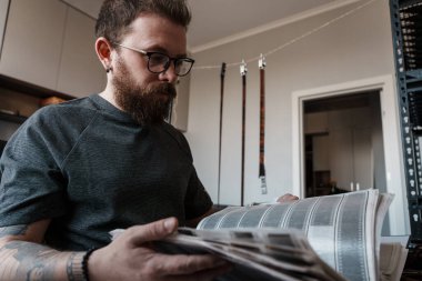 Odaklanmış sakallı adam, arka planda ekipmanlarla modern bir fotoğraf stüdyosunda film negatiflerini yoğun bir şekilde eleştiriyor..