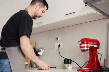Makarna hazırlamak için kırmızı bir karıştırıcı kullanarak modern bir mutfakta odaklanmış bir adam..