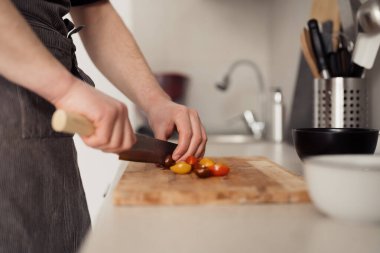 Bir adamın ellerinin domatesleri kestiği yakın plan bir mutfakta..