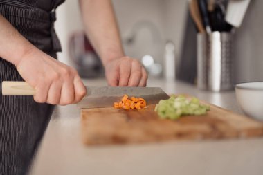Close-up of hands chopping fresh vegetables on a wooden cutting board in a home kitchen. clipart