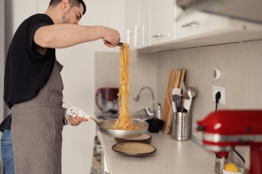 Modern mutfakta spagetti pişiren önlüklü adam, ev yemeklerine odaklan.