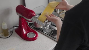 Bir insan eli, ev yapımı mutfak ortamında ev yapımı hamur yapmak için kırmızı makarna makinesi kullanıyor..
