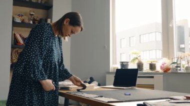 Profesyonel kadın moda tasarımcısı. Tekstil malzemelerini iyi aydınlatılmış yaratıcı bir stüdyoda cetvelle birlikte çalışıyor..
