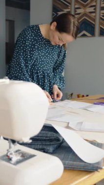 Kendini işine adamış bir kadın, kumaş ve desenlerle çevrili aydınlık bir odada dikiş dikerken görülüyor..