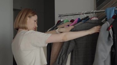 Modern bir yatak odasındaki gardıroptan kıyafet seçen bir kadın. Moda, organizasyon ve kişisel tarz kavramı.
