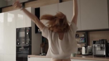 Neşeli bir kadın, parlak ve modern bir mutfakta coşkuyla dans ediyor. Görüntü mutluluk, hareket ve kaygısız yaşam anlarını yakalar..