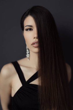 Sofistike siyah bir elbise giyen zarif bir kadını gösteren bir resim. Esmer, nötr bir arkaplana karşı poz veriyor. Gizem ve klas hissi yayıyor..