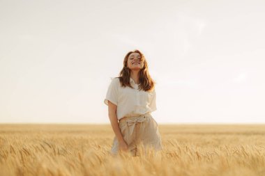 Muazzam bir buğday tarlasının ortasında altın saatin sıcağında güneşlenen bir kadının huzur ve memnuniyet hissi uyandırdığı sakin bir sahne..