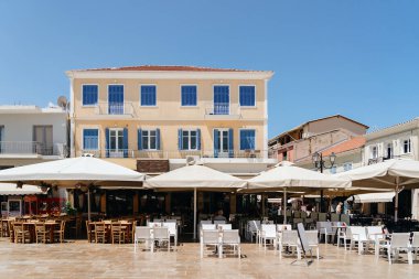 Beyaz şemsiyeler, geleneksel mimari ve açık mavi gökyüzü altında açık hava koltukları olan parlak ve davetkar bir Akdeniz kafesi..