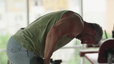 Bu resimde, bir adam spor salonunda dambıllarla egzersiz yapıyor, güç antrenmanına ve kas geliştirmeye odaklanıyor..