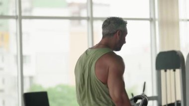 Spor salonunda ağırlık tabağını kafasının üzerine kaldıran bir adam. Güç antrenmanına ve forma odaklanıyor..
