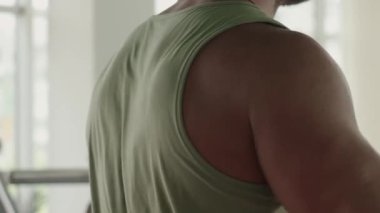 Spor salonundaki kaslı bir adamın güç antrenmanından önce ısınma egzersizleri yaptığı yakın çekim görüntüsü. Omuz ve üst kol kaslarına odaklan..