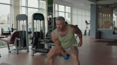 Spor kıyafetleri giyen bir adam modern bir spor salonunda kettlebell salıncak egzersizi yapar..