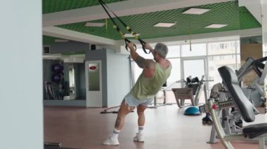 Formda bir adam modern bir spor salonunda güç eğitimi için süspansiyon antrenörü kullanıyor. Fitness ve kas geliştirmeye odaklanmış.