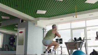 Bir adam, iyi donanımlı, modern bir spor salonunda atlama egzersizi yapıyor..