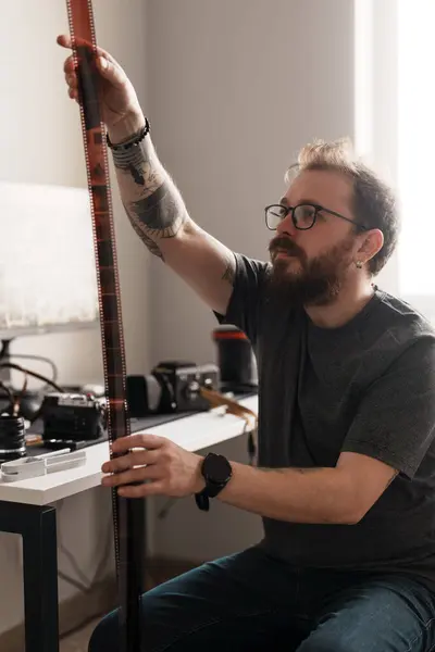 stock image Focused artist holds and inspects film strips carefully in a bright, modern workspace surrounded by photography equipment.