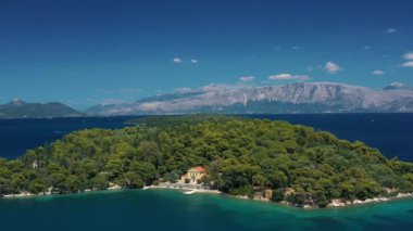 Gök mavisi denizle çevrili yemyeşil bir adada özel bir villanın dingin güzelliğini gösteren bir hava manzarası..