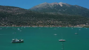 Bereketli yeşil dağlar ve berrak gökyüzünün zeminine demirlemiş teknelerle sakin bir koy manzarası..