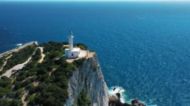 Derin mavi bir denizin üzerindeki kayalık bir uçuruma tünemiş beyaz bir deniz fenerinin havadan görünüşü rehberlik ve sükunet hissini yakalıyor..