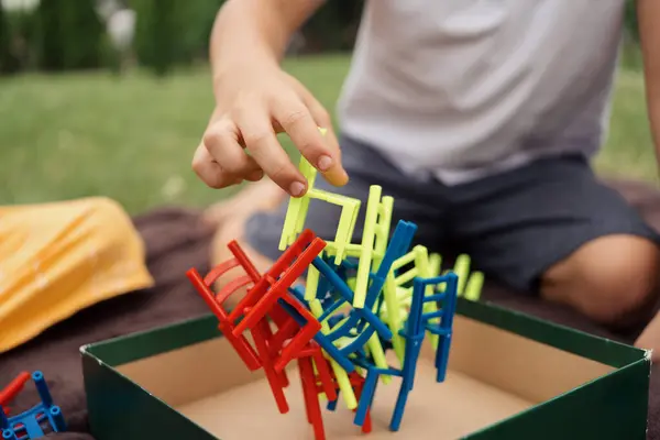 stock image A child is playing with a colorful stacking toy in an outdoor setting. The hands carefully balance the pieces.