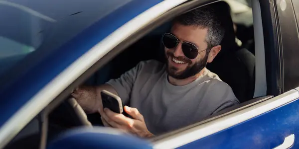 stock image A man in a blue electric vehicle is engaged with his smartphone, showcasing modern connectivity and electric mobility.